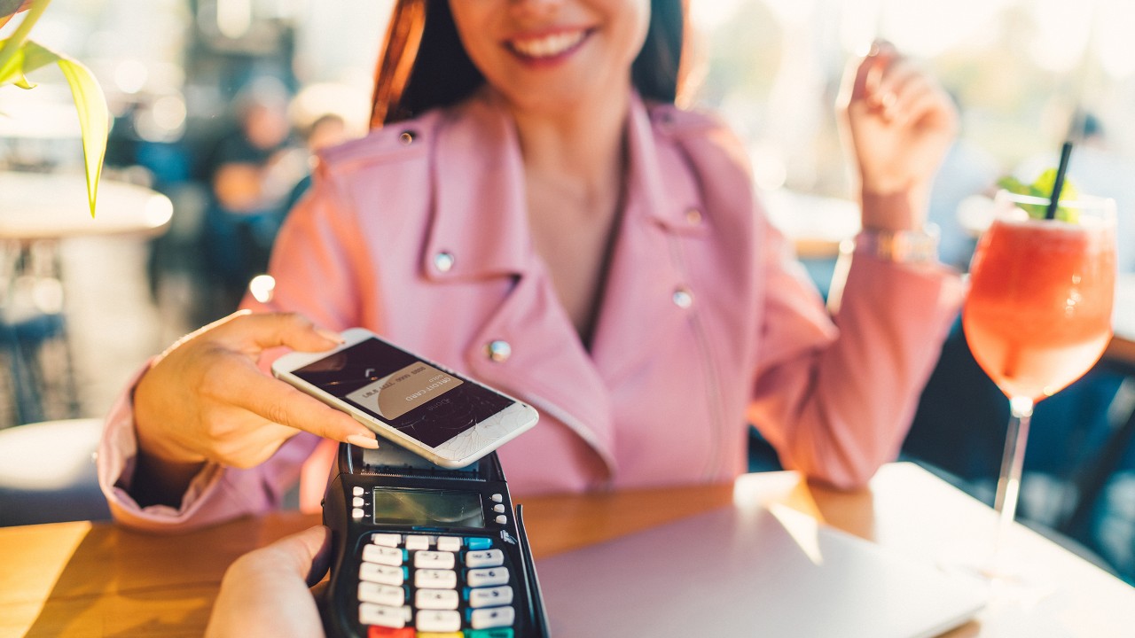 A smiiling woman is using contactless payment with smartphone; image used for HSBC Mobile Payment Services.