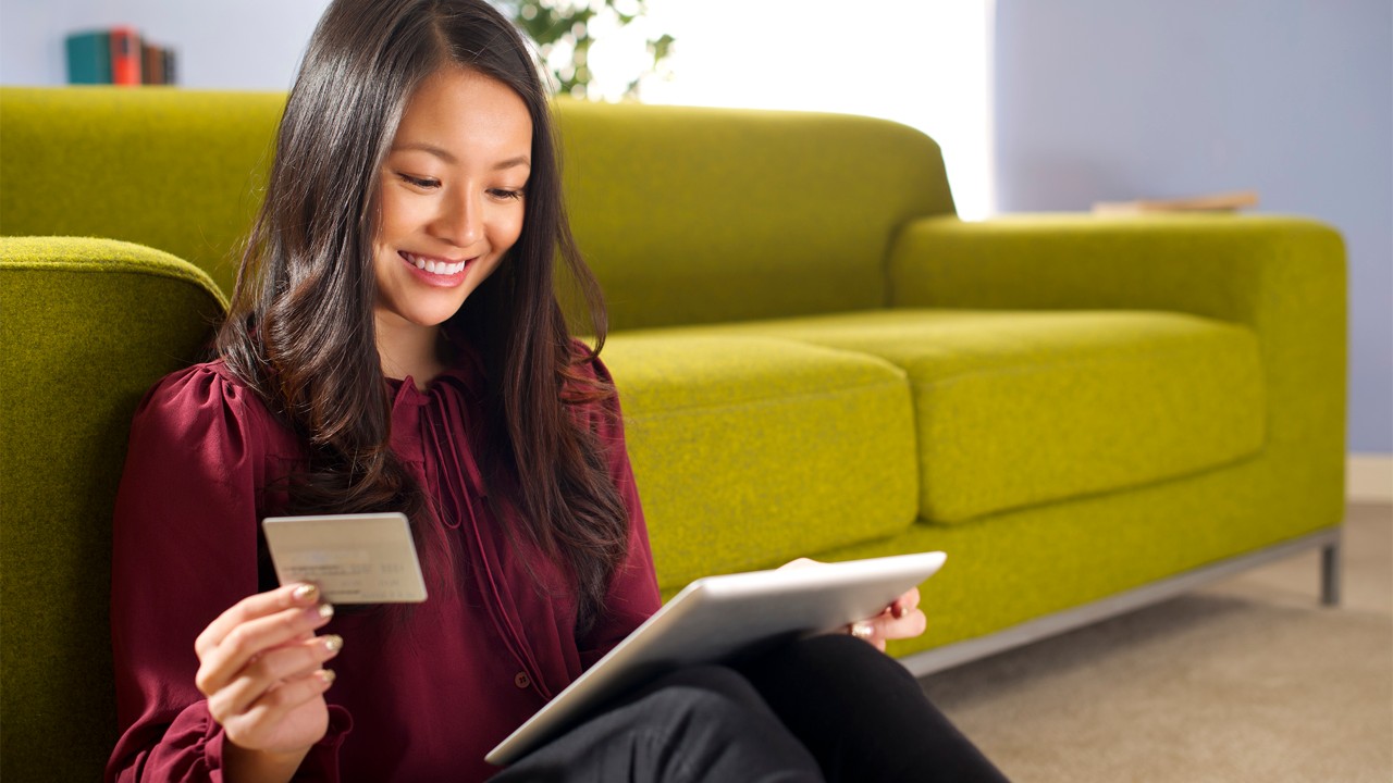 A woman is using her tablet and credit card; image used for Online Card Activation.