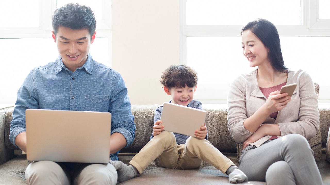 A family sitting on sofa to playing mobile device; image used for HSBC Children Savings Account.