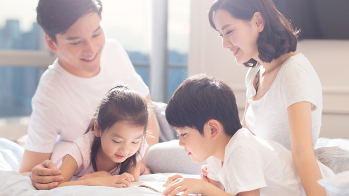 Happy family is reading books in bed; image used for Income Goal Insurance Plan.