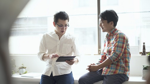 A man is holding his tablet while talking to his male friend; image used for HSBC Wealth Management page.