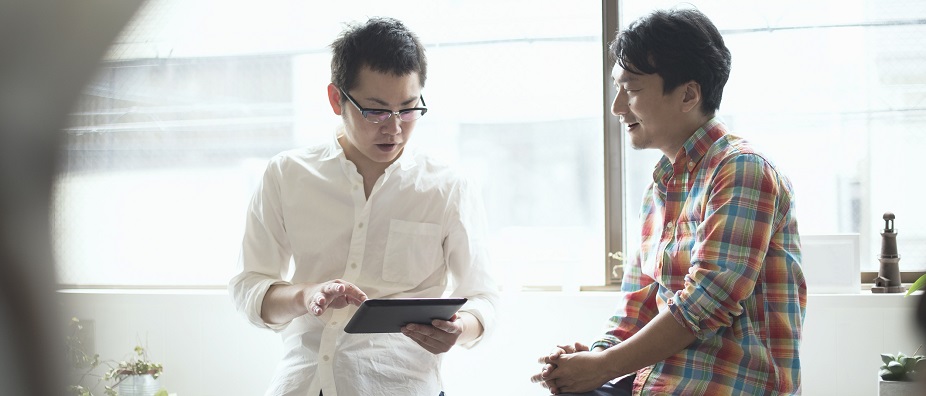 A man is holding his tablet while talking to his male friend; image used for HSBC Wealth Management page.