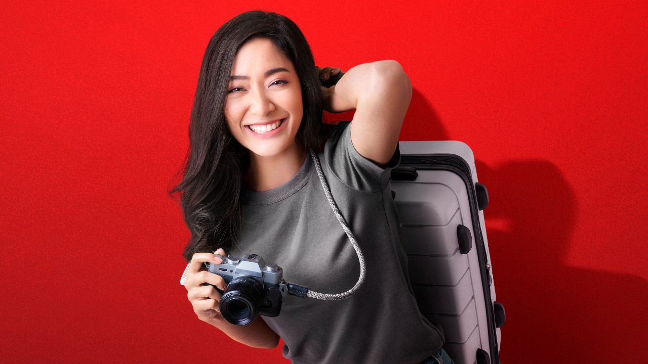 Happy young lady holding a suitcase and a camera; image used for HSBC One