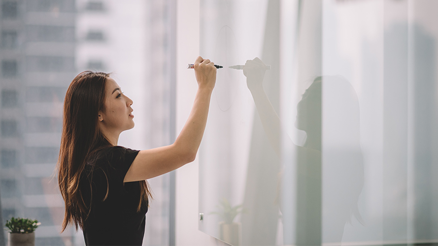 A woman is writing her plan on the white board; the image is used for How to set a budget, repay debt and reach your financial goals" article.