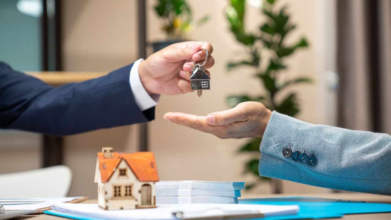 Estate agent giving house keys to a man and sign agreement in office; image used for HSBC ResidenceSurance.
