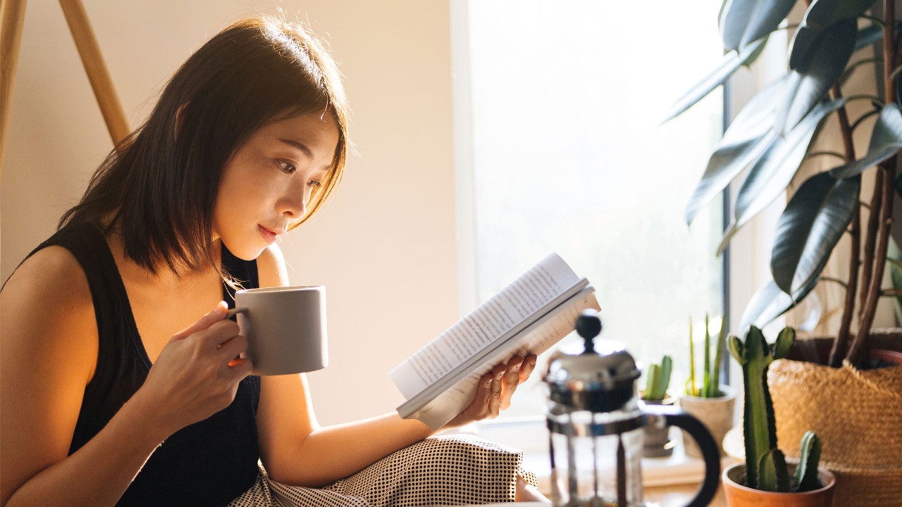 woman holding a cup and reading a book