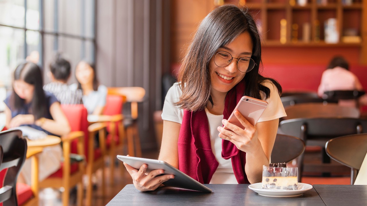 一位微笑的女士在咖啡厅查看手机；图片用于汇丰香港微信页面。
