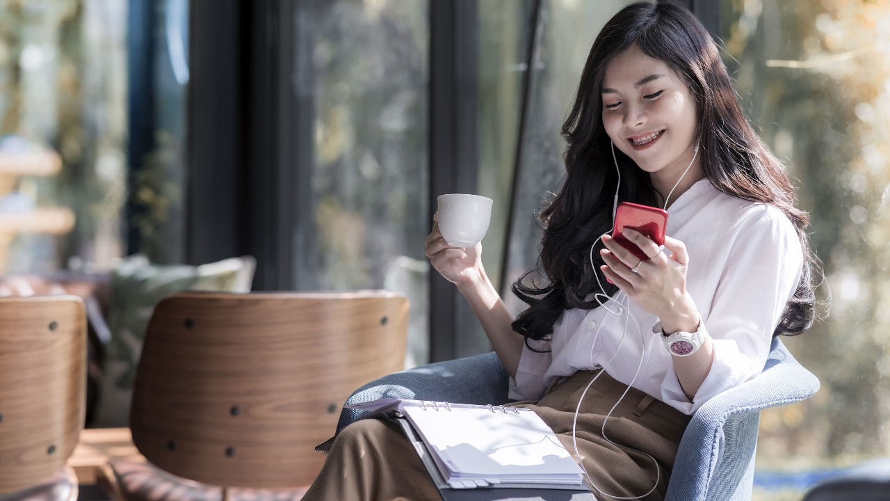 lady happily listening songs and holding a cup in a cafe