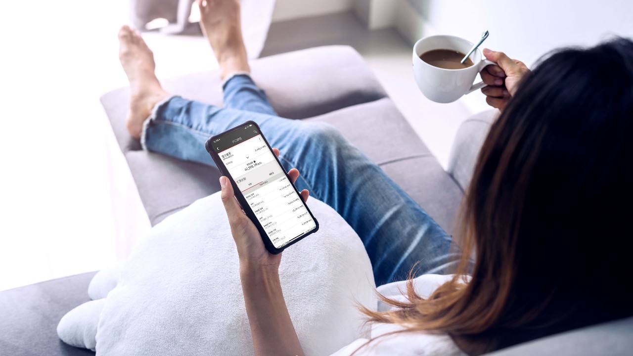 A lady is drinking coffee while looking at her mobile phone.