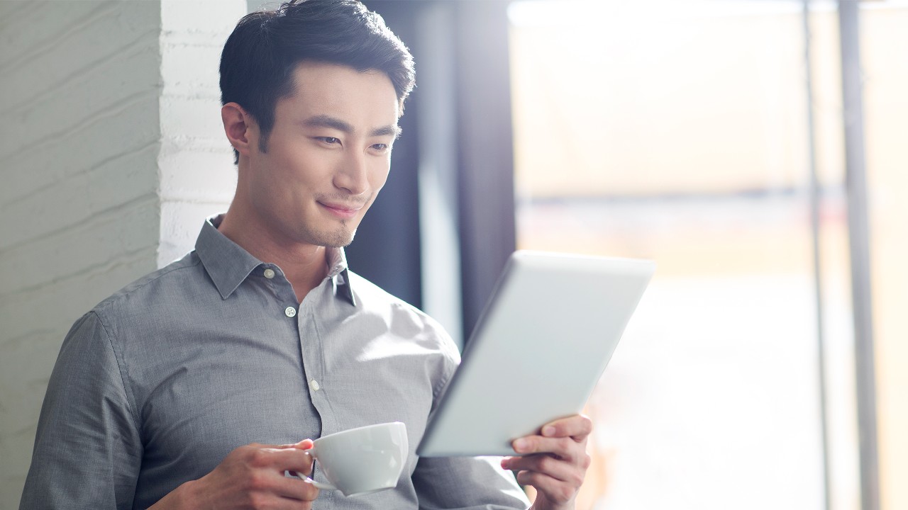 Man reading on his tablet while holding a coffe cup; image used for HSBC Wealth Portfolio Intelligence Service
