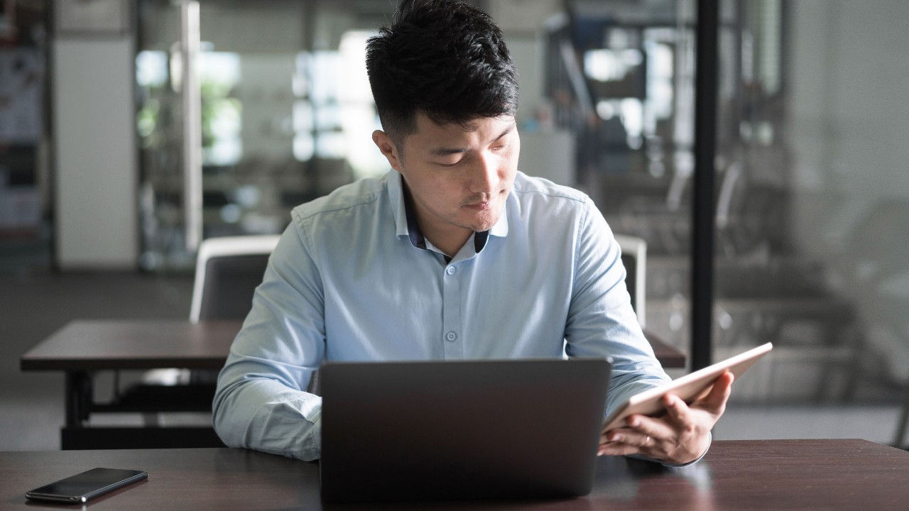 a man sitting in a office and looking at his laptop and tablet; image used for HSBC ELI