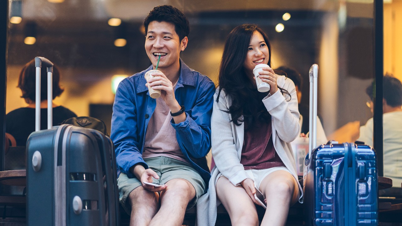 一对情侣开心地饮用外带咖啡,等候上机;图片使用于汇丰保本投资存款 - 货币挂钩III