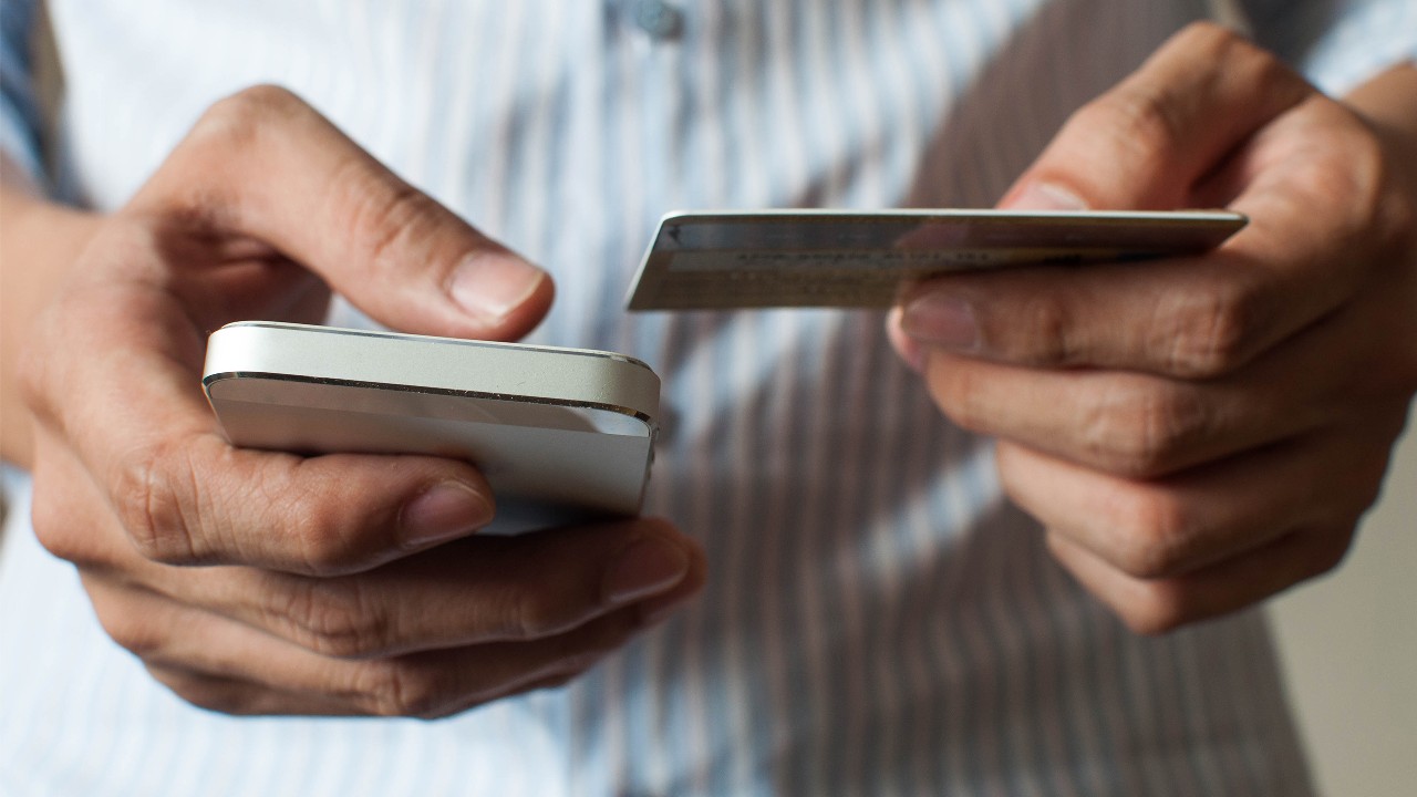A businessman is using his mobile phone and holding a credit card; image used for navigation of online and mobile banking pages.