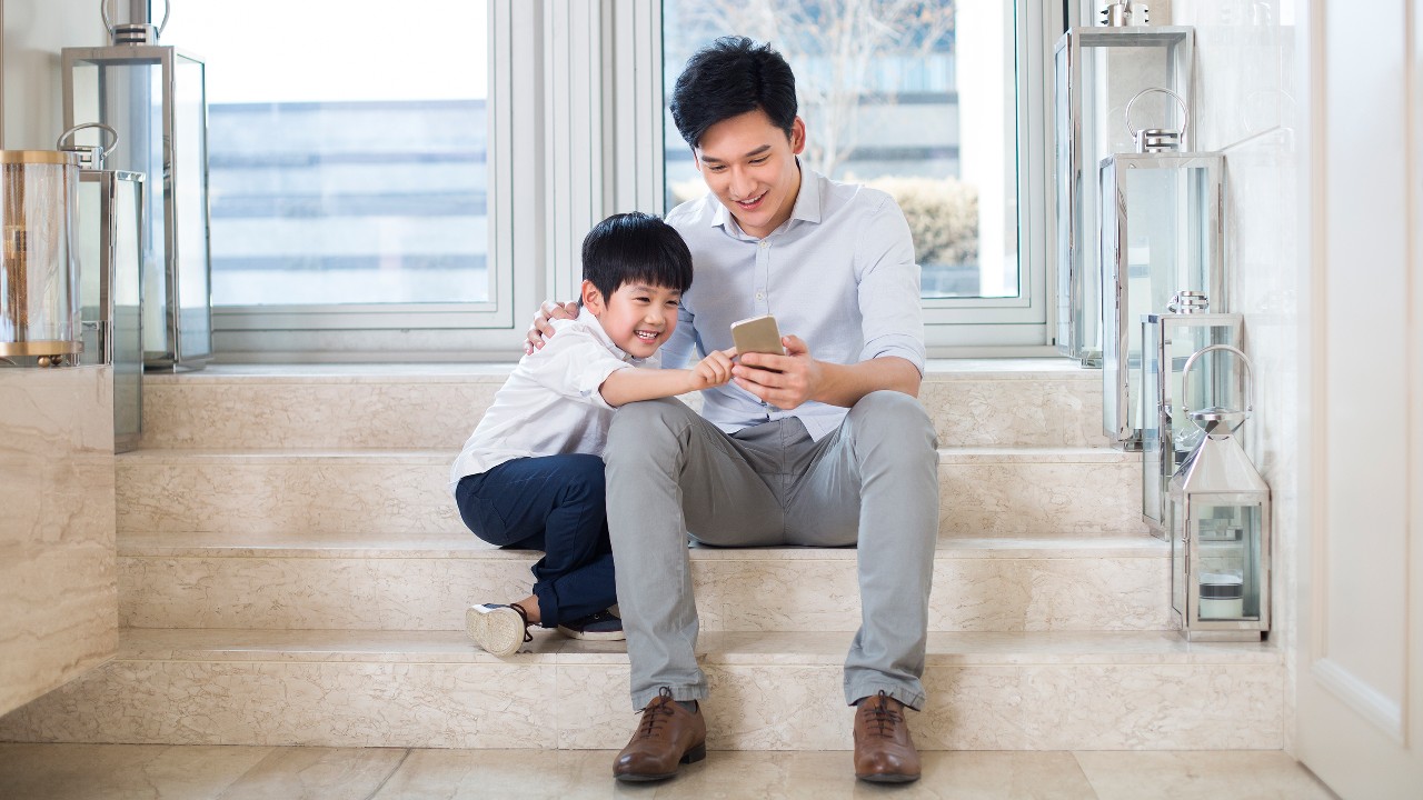 Father and son using mobile phone together; image used for navigation to banking security pages.