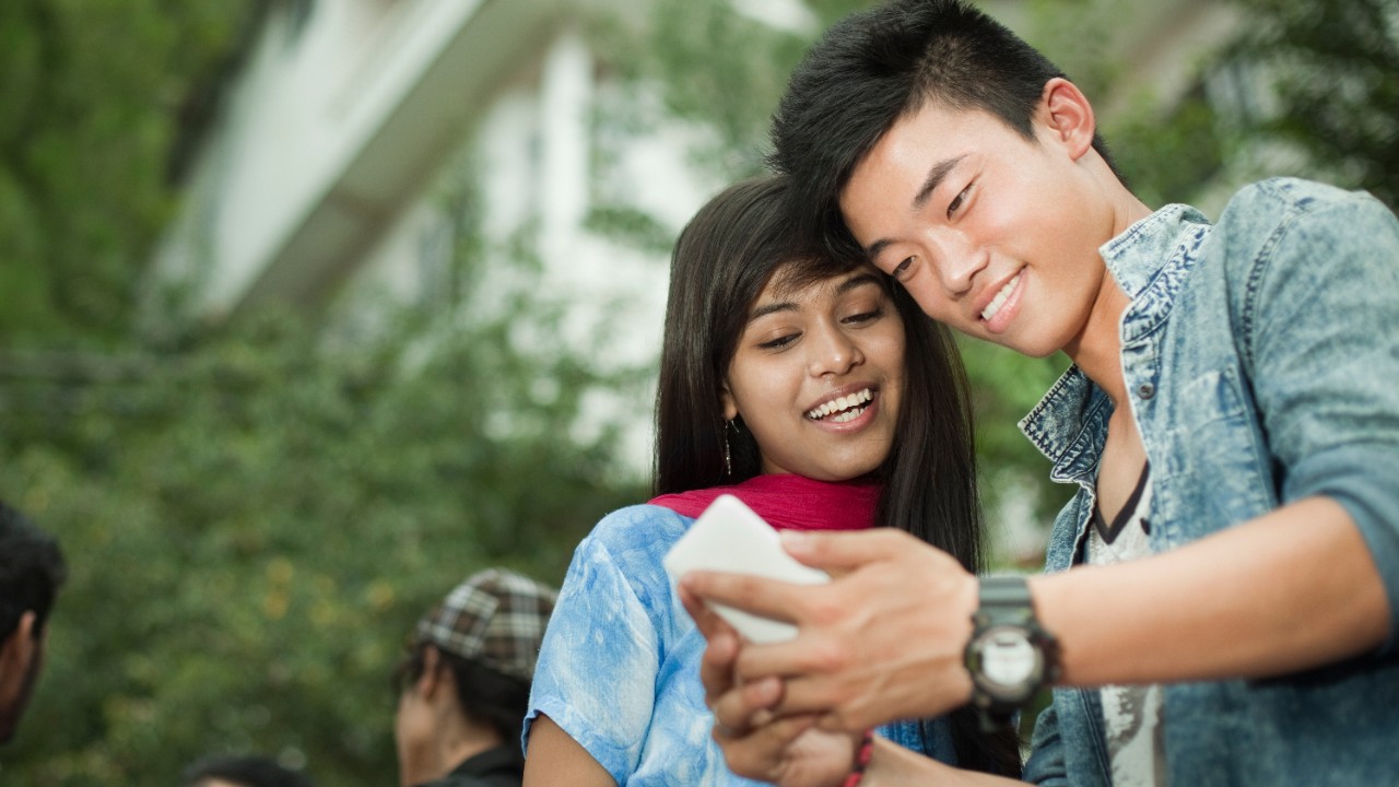 A couple is checking online banking services on a mobile phone; image used for HSBC Local Money Transfer