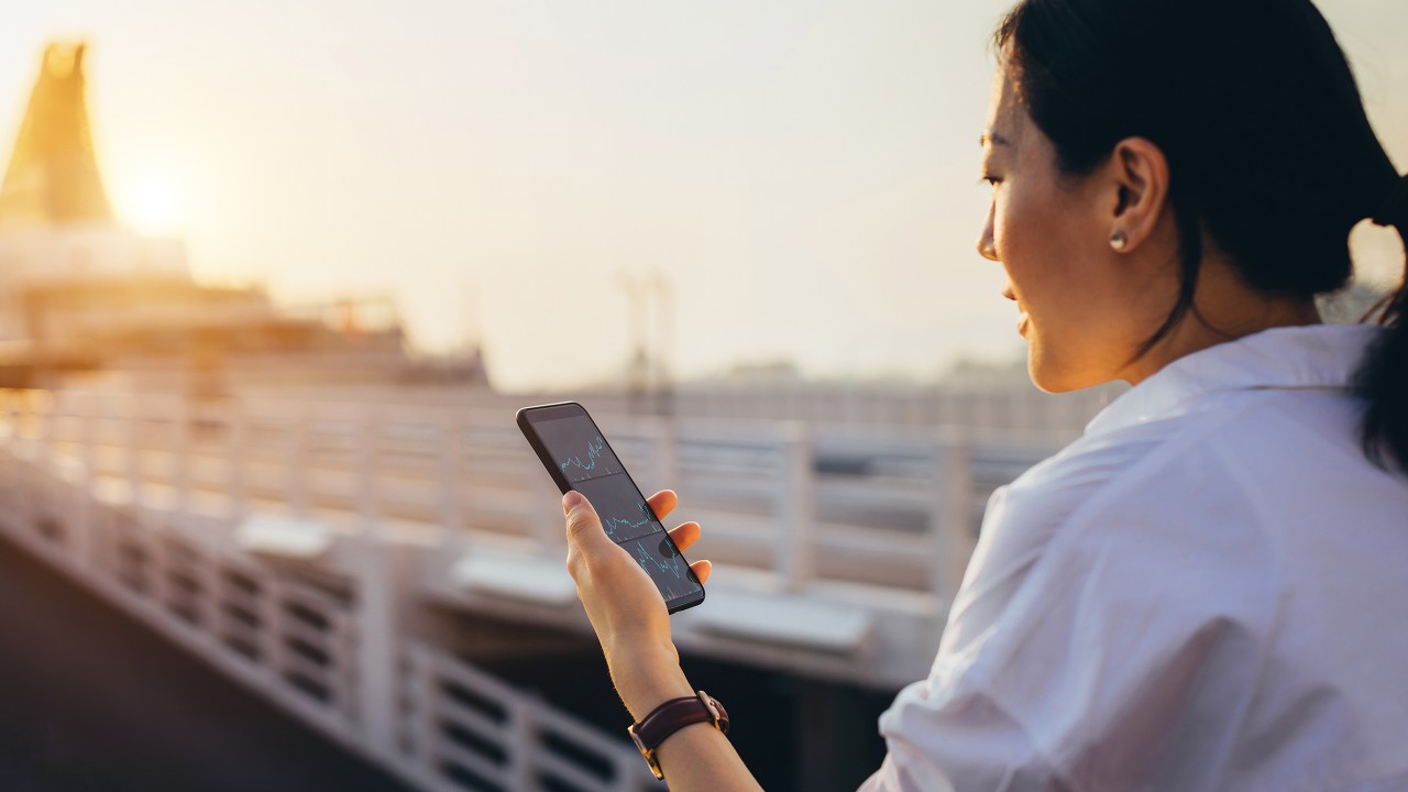 A woman is using her phone to browse investment news; image used for the HSBC Hong Kong WeChat page.