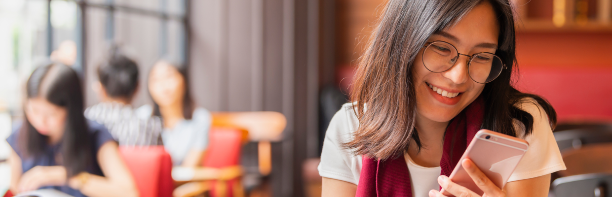 A smiling woman is looking at her phone while holding a tablet; image used for the HSBC Hong Kong WeChat page.